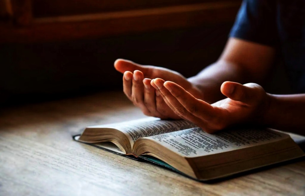Pair of hands praying over a Bible