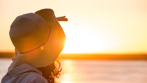 Young and beautiful woman wearing a hat in sunset light looking far away. Photo from behind