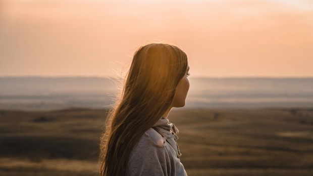 Woman in grey hoodie standing on beach during sunset
