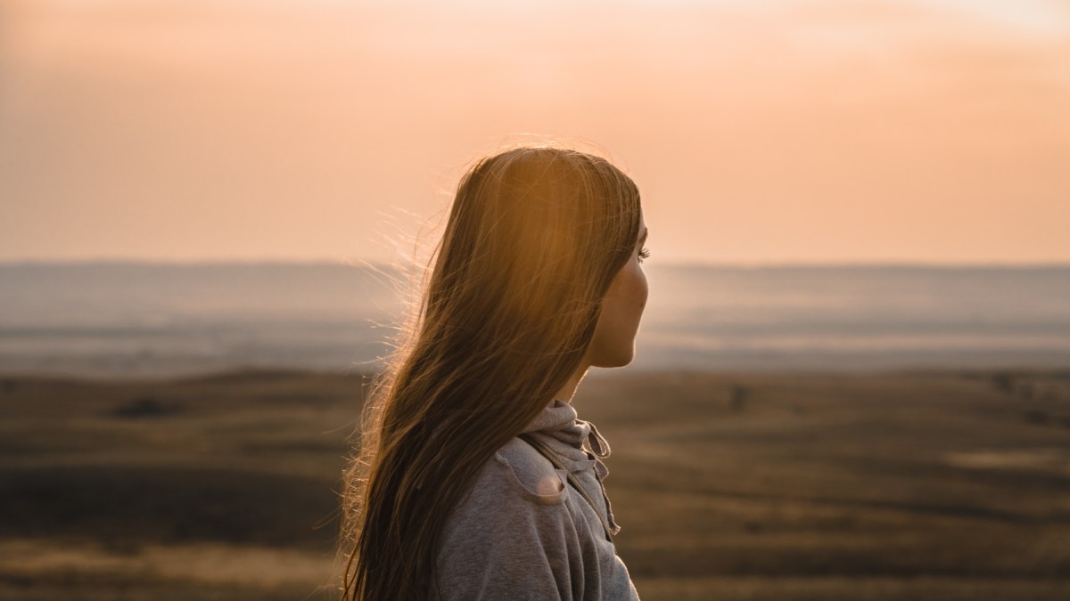 Woman in grey hoodie standing on beach during sunset