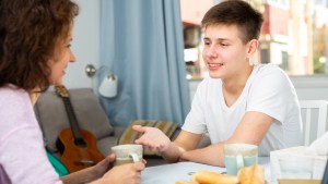 Portrait of happy teenager having friendly chat with his mom at home