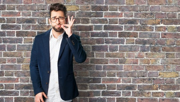 Mężczyzna na tle ceglanej ściany udaje, że zamyka sobie usta.