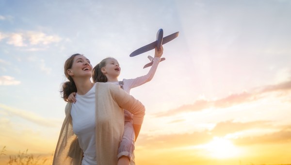Happy family, mother and kid with toy plane are running through the field at sunset