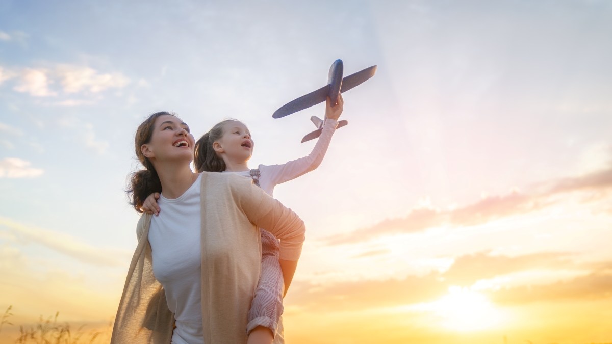 Happy family, mother and kid with toy plane are running through the field at sunset