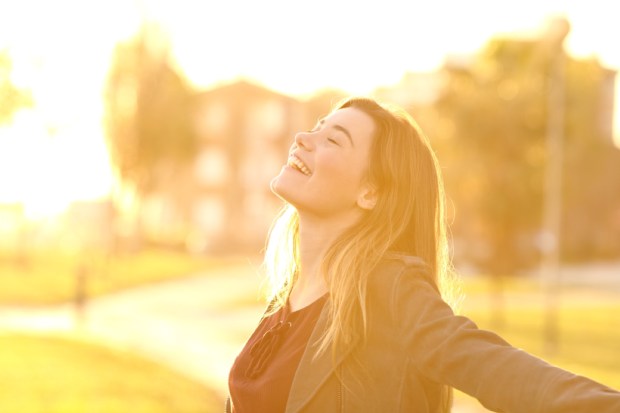 Back light portrait of a happy single teen girl breathing fresh air at sunset in a park
