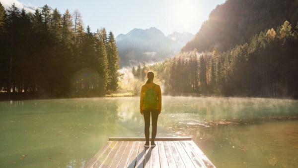 Young woman standing at the edge of a wooden pier at a mountain lake