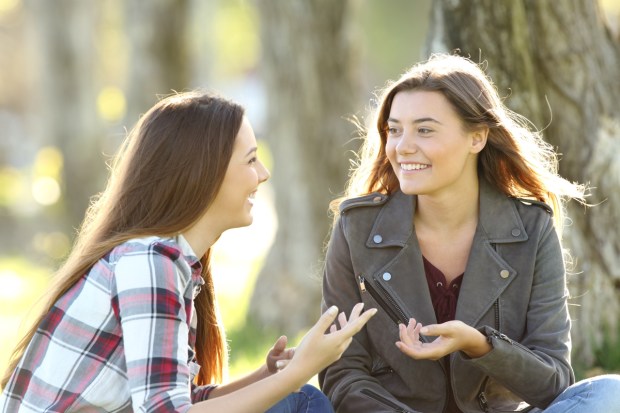 Two friends talking and laughing sitting on the grass in a park