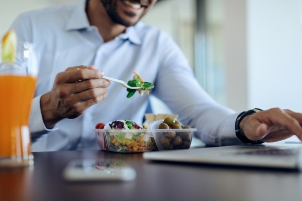 Close-up of businessman eating healthy food while using computer on lunch break in the office