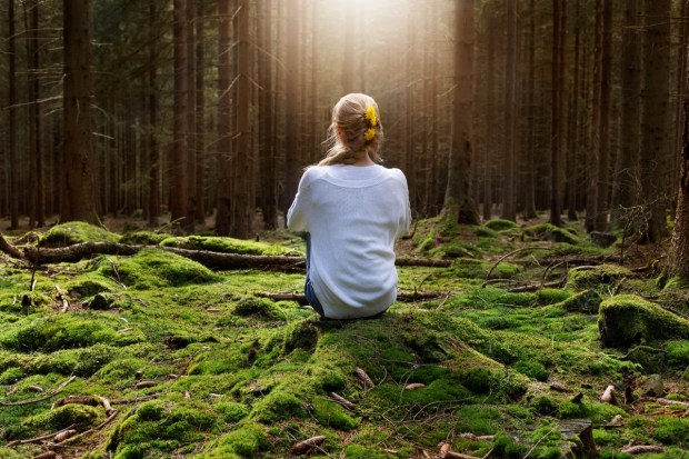 Woman sitting in forest enjoys the silence and beauty of nature