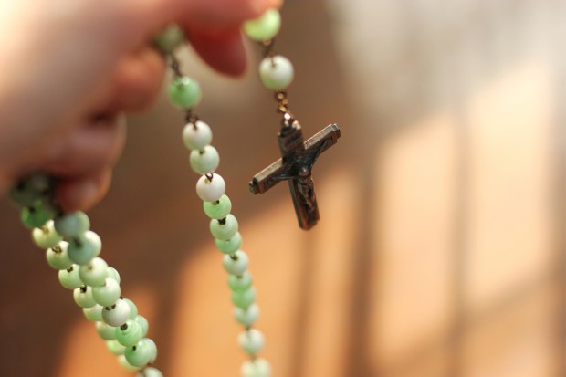 holy rosary with hand to pray with light and shadows in dark tone background