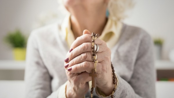 Starsza kobieta modli się na różańcu