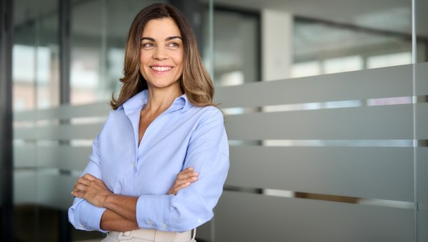 Happy confident mature professional business woman standing at work in office arms crossed looking away