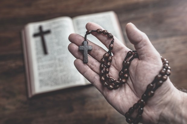 Dłoń z różańcem na tle otwartej Biblii
