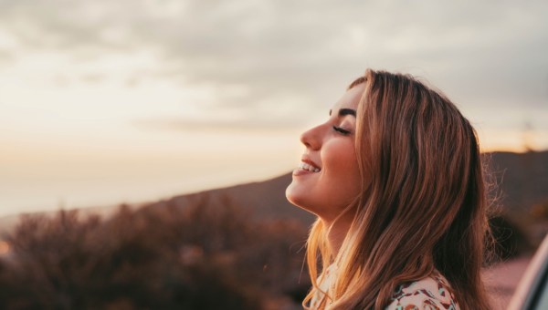 Piękna kobieta z zamkniętymi oczami i uśmiechem wystawia twarz na słońce