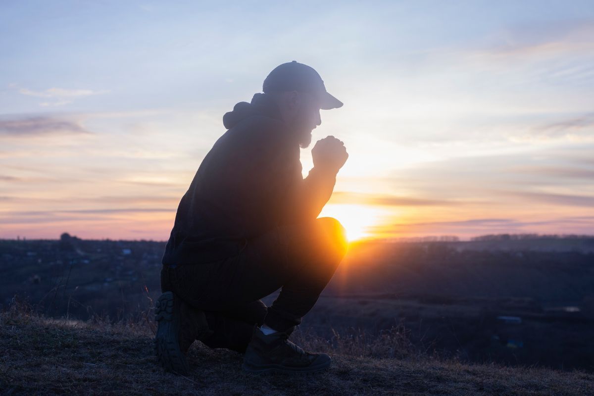 Prayer. Man on his knees praying. On the background of the sunset sky. Kneeling Prayer to God. Worship and praise.